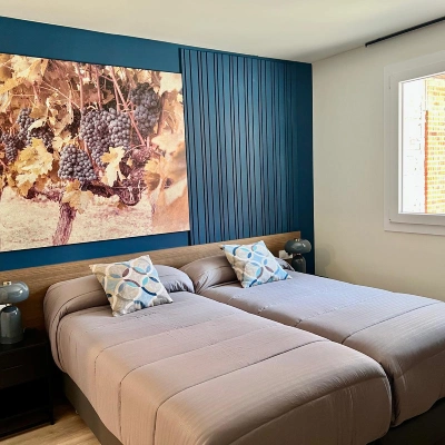 Dormitorio con cama doble, cojines y ventana, pared con fotograf&iacute;a y cortinas azules