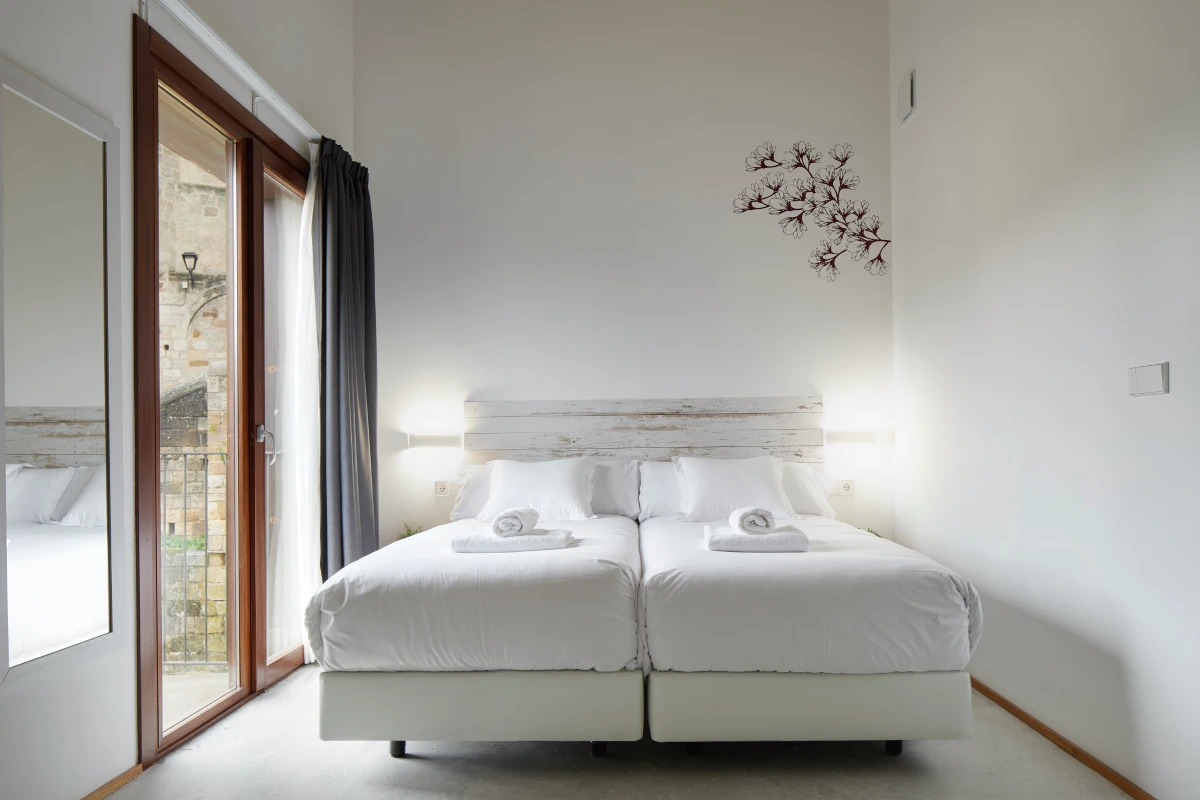 Dormitorio moderno con cama doble blanca y puerta al exterior con luz natural
