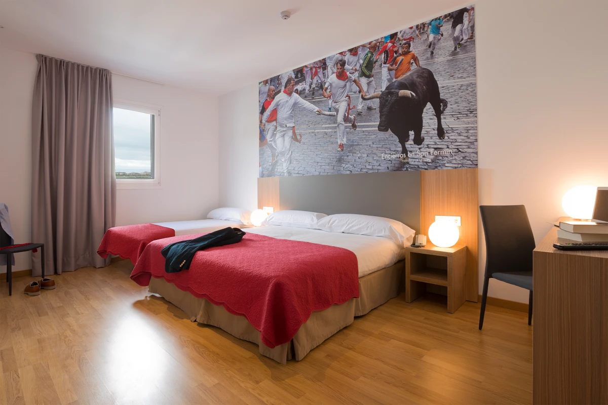 Dormitorio moderno con cama roja, mesilla y foto grande de encierro con toros