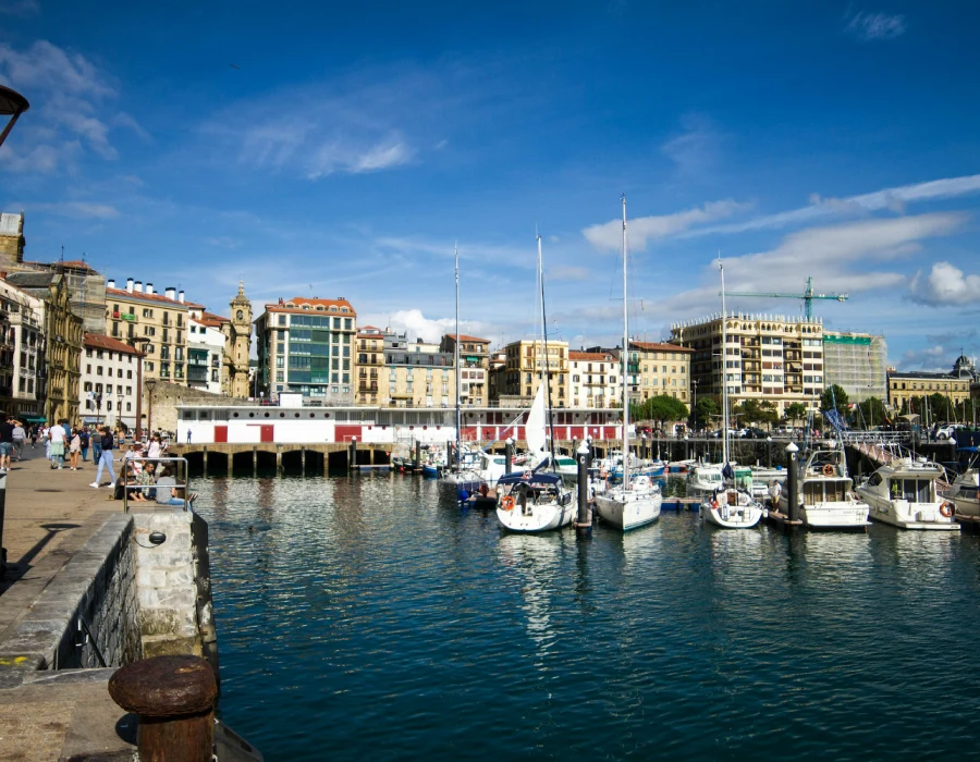 Puerto con veleros amarrados y edificios mediterr&aacute;neos bajo cielo azul