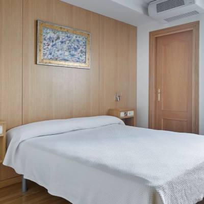 Habitaci&oacute;n con cama, mesilla, cuadro y puerta de madera.
