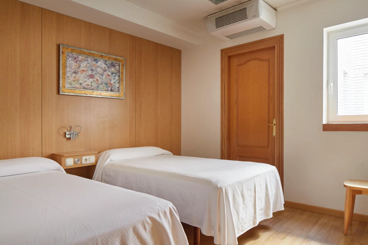 Habitaci&oacute;n con dos camas, cuadro, puerta de madera y ventana con persiana