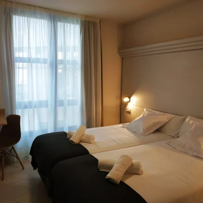 Habitaci&oacute;n de hotel con cama, cojines y cortinas junto a una ventana