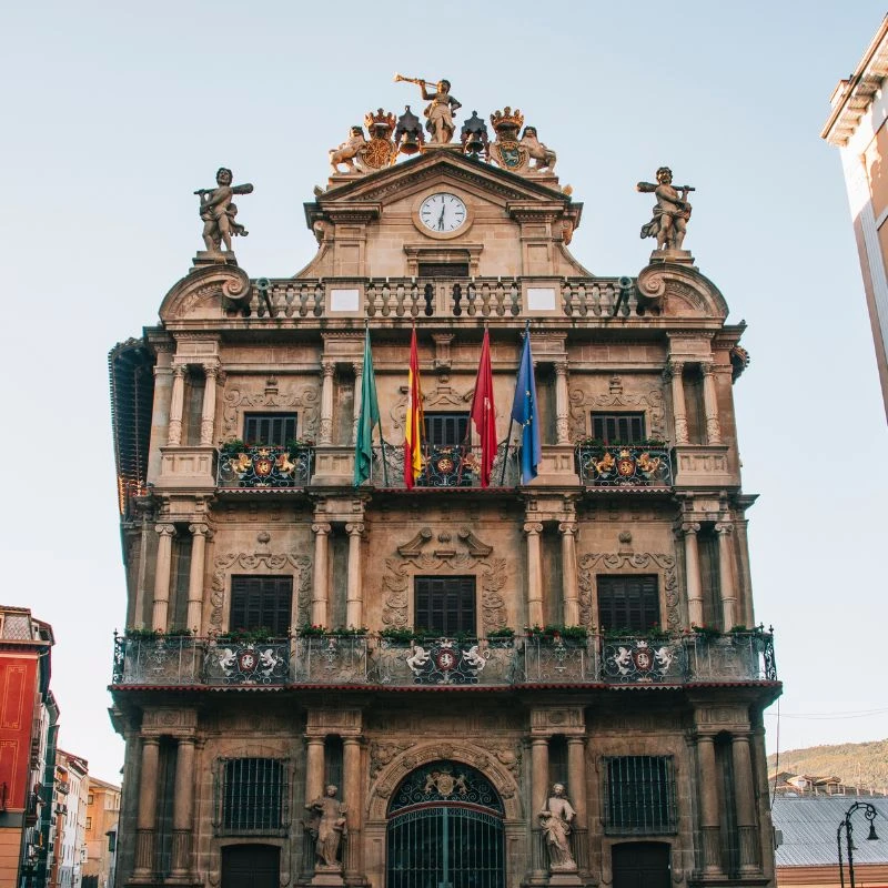 Fachada de un edificio hist&oacute;rico con reloj, estatuas y banderas en la cima