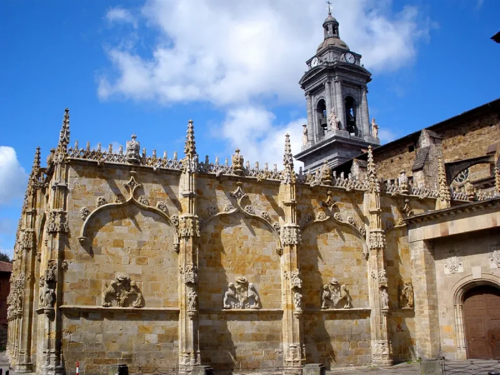 Fachada de piedra con capilla g&oacute;tica y campanario bajo cielo azul