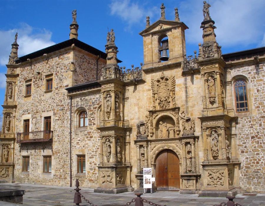 Fachada hist&oacute;rica de piedra con campana y estatuas bajo cielo azul.