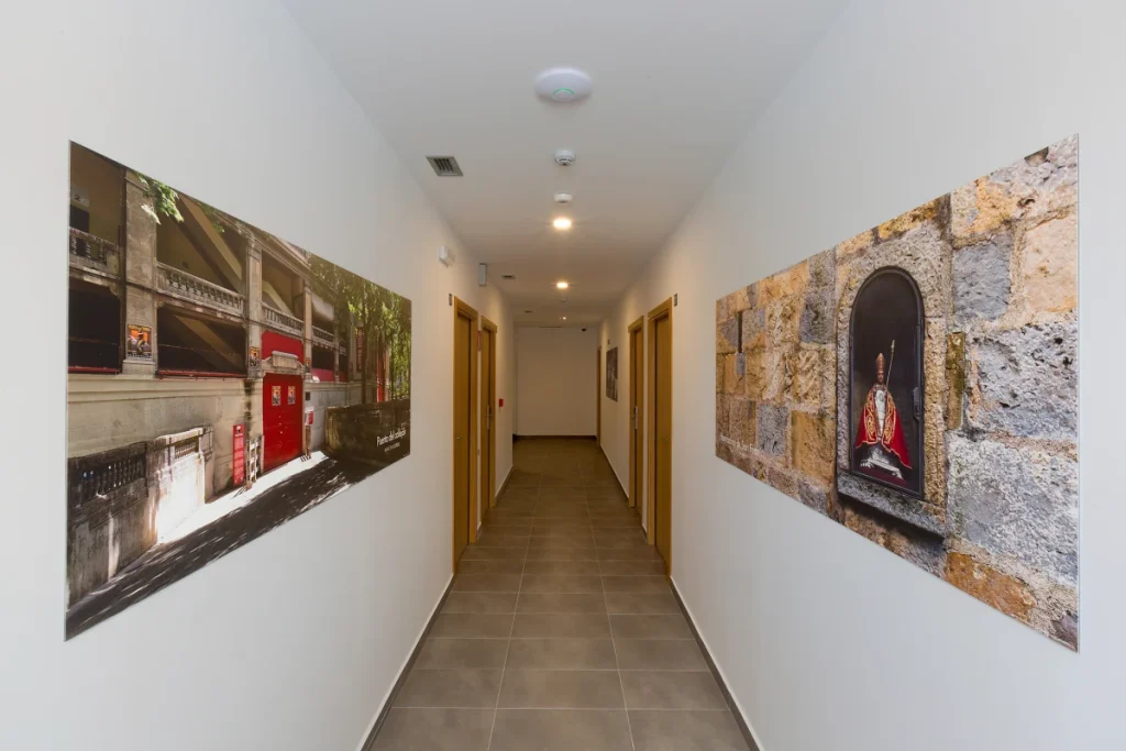 Pasillo interior con azulejos grises y cuadros en las paredes, luz del techo.