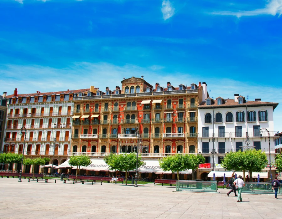 Fachada hist&oacute;rica con balcones y plaza frente a cielo azul en Espa&ntilde;a