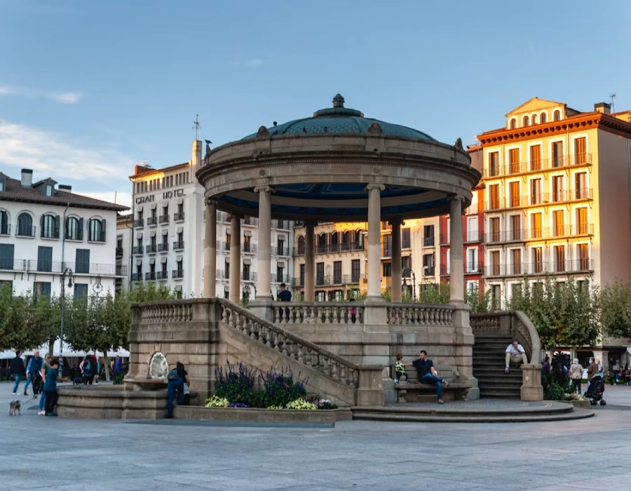 Fuente circular con c&uacute;pula y edificios de colores en una plaza urbana