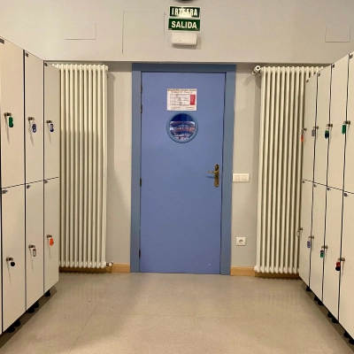 Pasillo con taquillas met&aacute;licas y una puerta azul al fondo.
