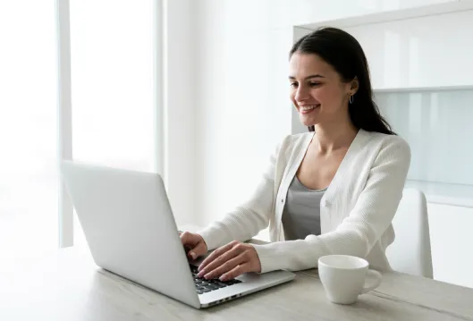 Mujer sonriente trabajando en laptop en oficina luminosa con taza de caf&eacute;