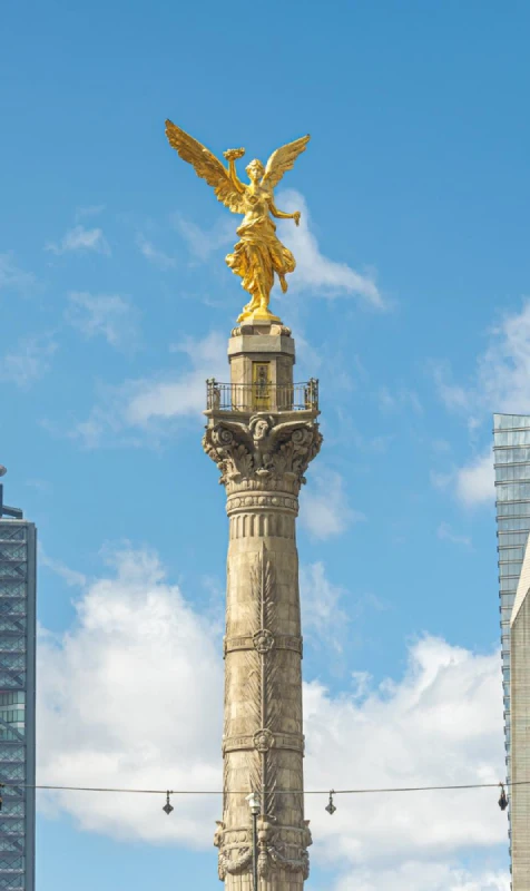 Estatua dorada de un &aacute;ngel sobre una columna con el cielo azul.