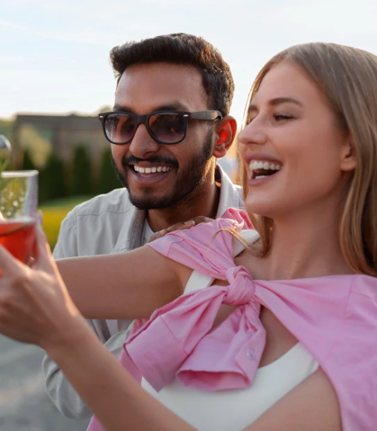 Pareja sonriente en una terraza al atardecer, con un beb&eacute; rosa en brazos