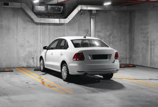 Auto blanco en estacionamiento subterr&aacute;neo con se&ntilde;alizaci&oacute;n amarilla.