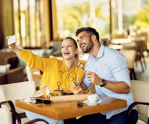 Pareja sonriente brinda en un caf&eacute; y hace una foto con el celular