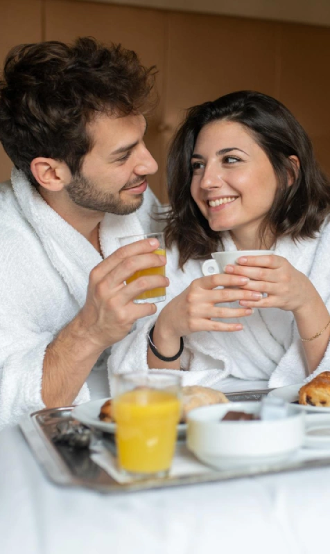 Pareja en bata sonriente desayunando, bebiendo jugo y caf&eacute; en bandeja