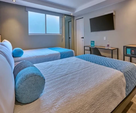 Dormitorio moderno con cama, almohadas azules y pantalla de TV en pared