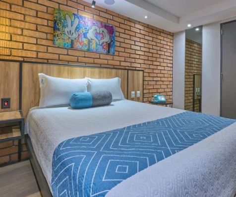 Dormitorio moderno con cama blanca, cojines y edred&oacute;n azul en sala de ladrillo