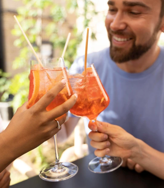 Dos hombres brindan con c&oacute;cteles de color naranja en una terraza al aire libre