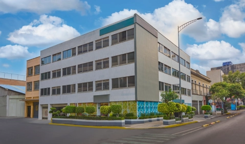 Edificio escolar moderno con jard&iacute;n y fachada colorida, junto a una calle