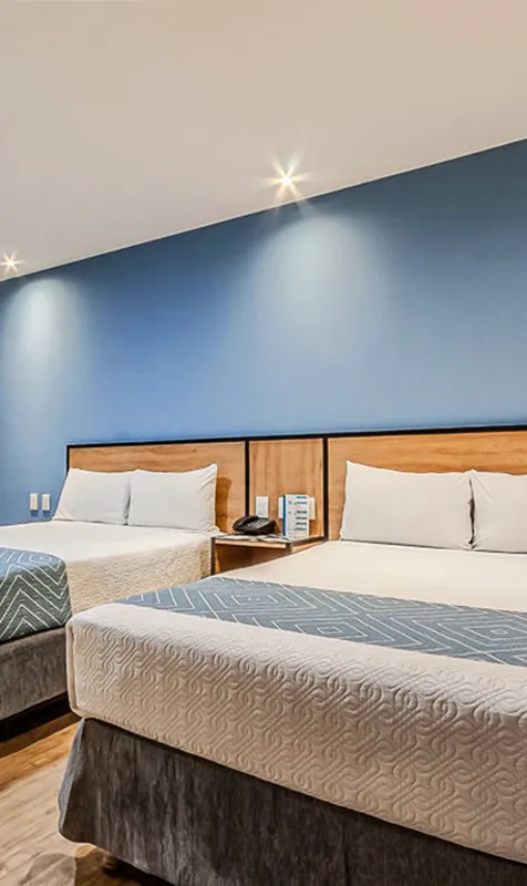 Tres camas con cabeceros de madera y s&aacute;banas azules en una habitaci&oacute;n moderna
