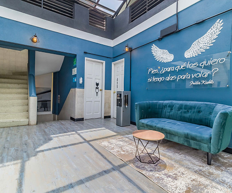 Pasillo azul con sof&aacute; turquesa y mural de &Aacute;ngel con cita de Frida Kahlo