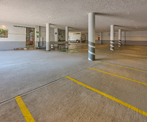 Estacionamiento subterr&aacute;neo con l&iacute;neas amarillas y columnas grises.