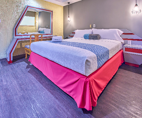 Dormitorio con cama doble, mesitas, alfombra morada y ventana en esquina
