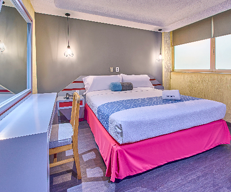 Dormitorio con cama doble, almohadas azules y cortinas en ventana.