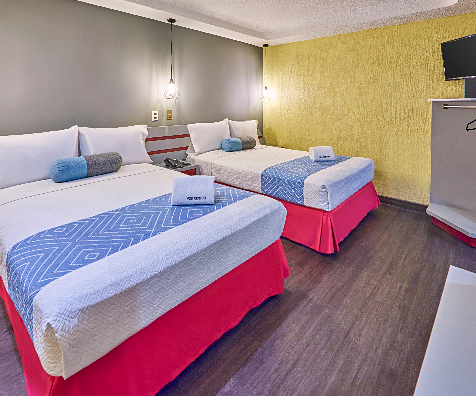 Habitaci&oacute;n con varias camas y cojines azules, paredes amarillas y grises.