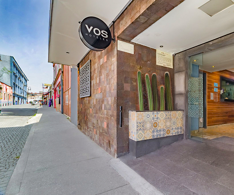Fachada del hotel VOS con pared de mosaicos y acceso en calle urbana