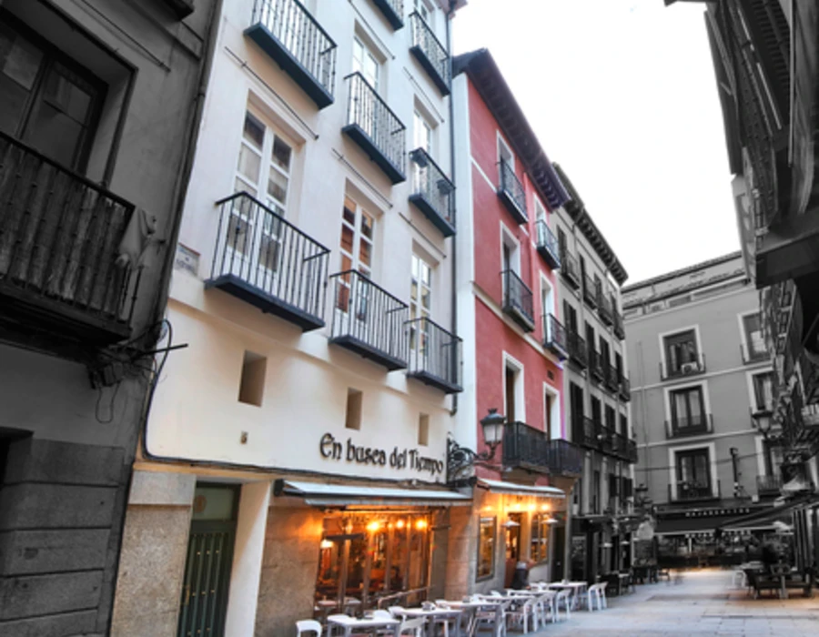 Calle estrecha con edificios de balcones y terraza con mesas al fondo