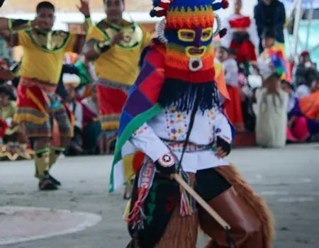 Bailarines con trajes coloridos y m&aacute;scara durante una celebraci&oacute;n.