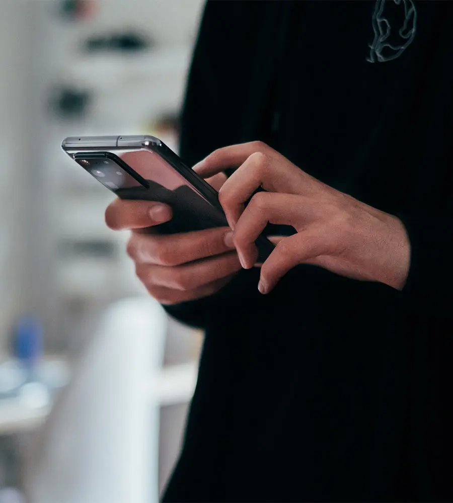Persona usando un tel&eacute;fono m&oacute;vil en interiores, manos sujetando el dispositivo