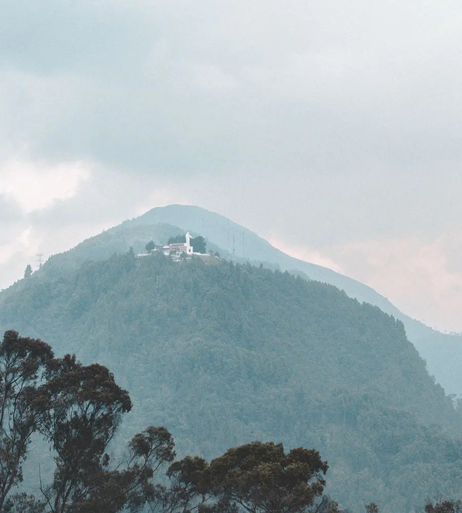 Monta&ntilde;a boscosa con una iglesia blanca en la cima, entre neblina