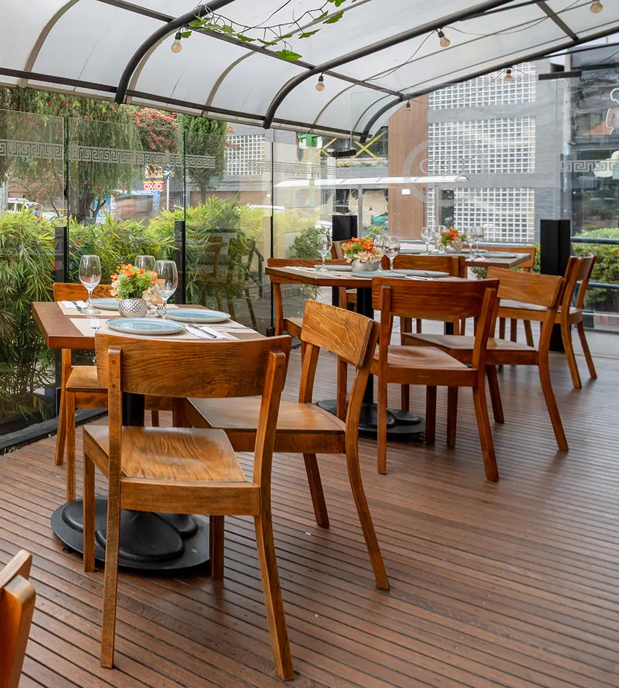 Mesa y sillas de madera en terraza con plantas y luz de guirnalda.