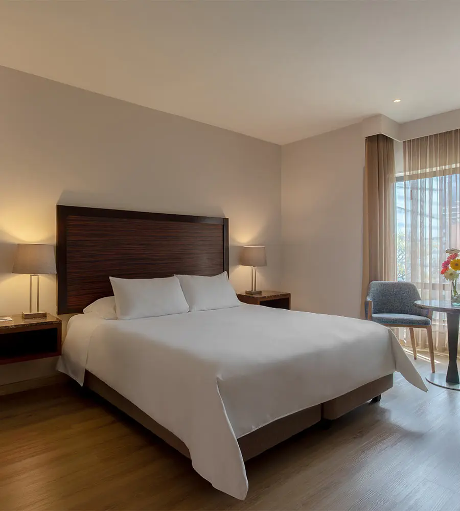 Habitaci&oacute;n de hotel moderna con cama doble, mesitas y l&aacute;mparas junto a ventana