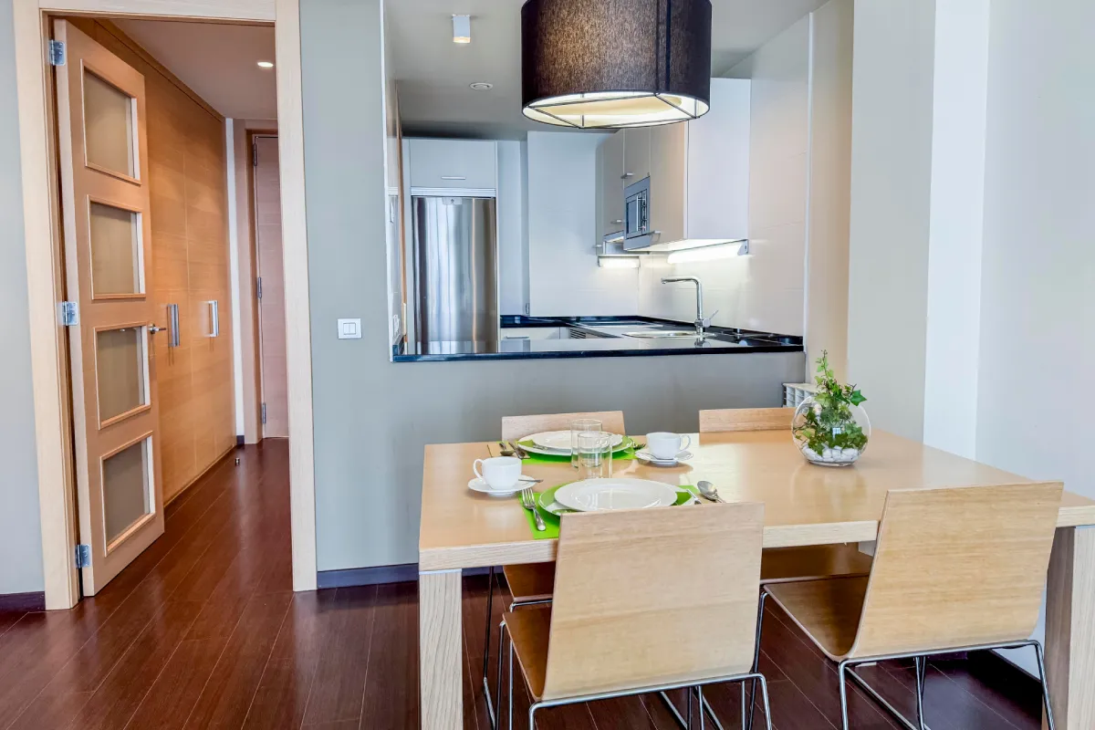 Comedor con mesa de madera, sillas, cocina integrada y lámpara colgante.