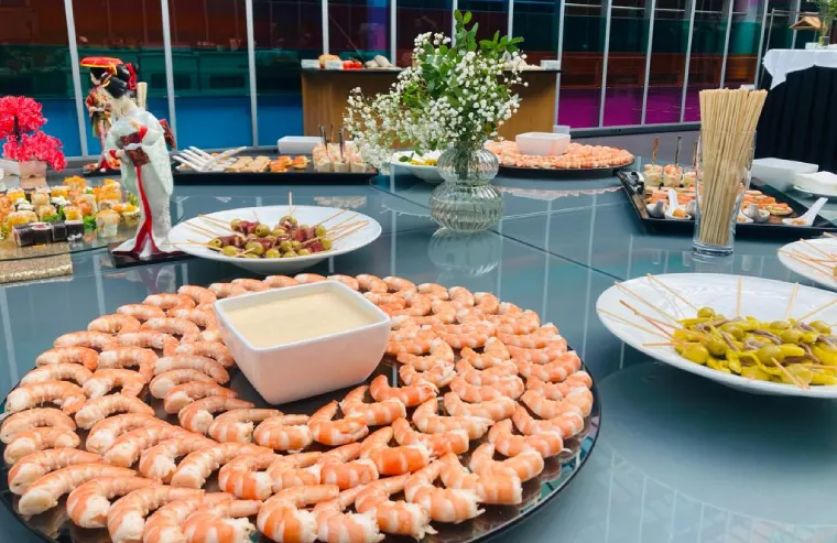 Mesa con bandejas de camarones y platos de ensaladas en buffet.