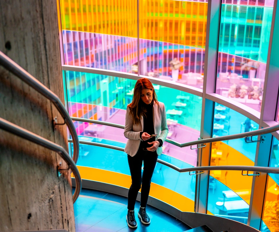 Mujer con m&oacute;vil en escaleras junto a paneles de colores brillantes.