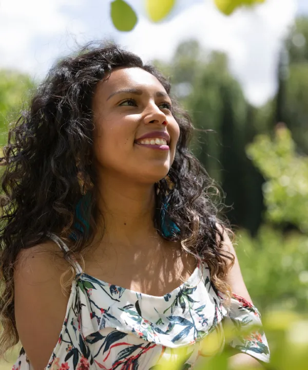 Mujer sonriente al aire libre con vestido estampado y pelo rizado.
