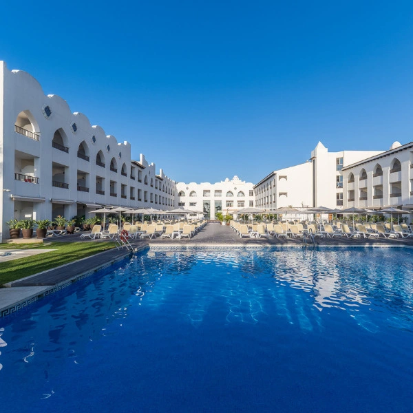 Piscina azul y fila de tumbonas en complejo hotelero con edificios blancos