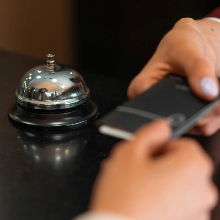 Mano presionando el timbre de recepci&oacute;n con un tel&eacute;fono en primer plano