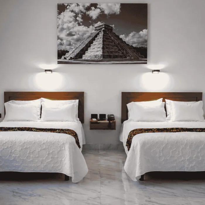Dos camas gemelas con almohadas blancas y cuadro de la pir&aacute;mide en la pared