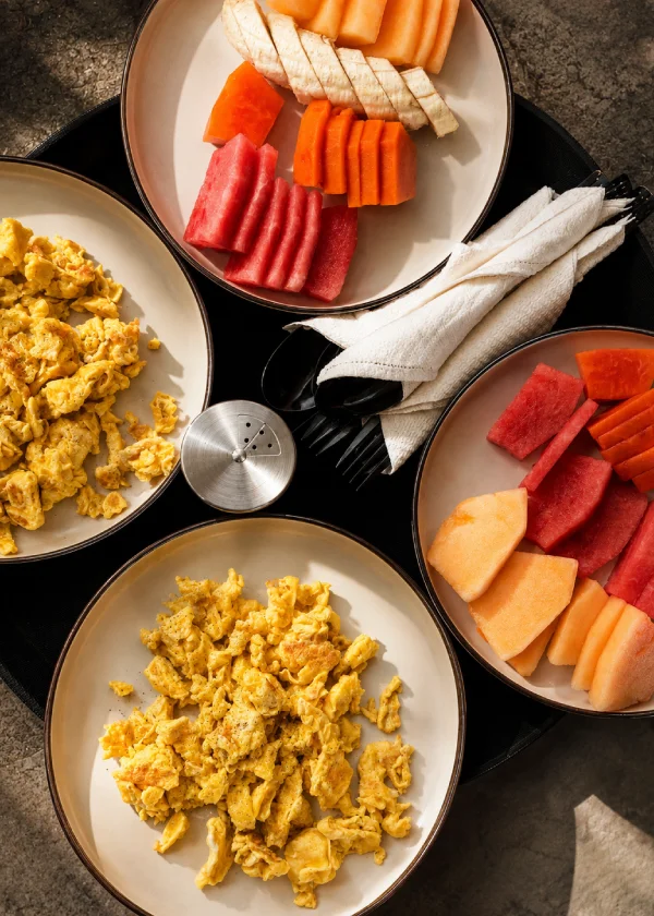 Platos con frutas y yogur: fresas, mel&oacute;n y papaya, y huevos revueltos.