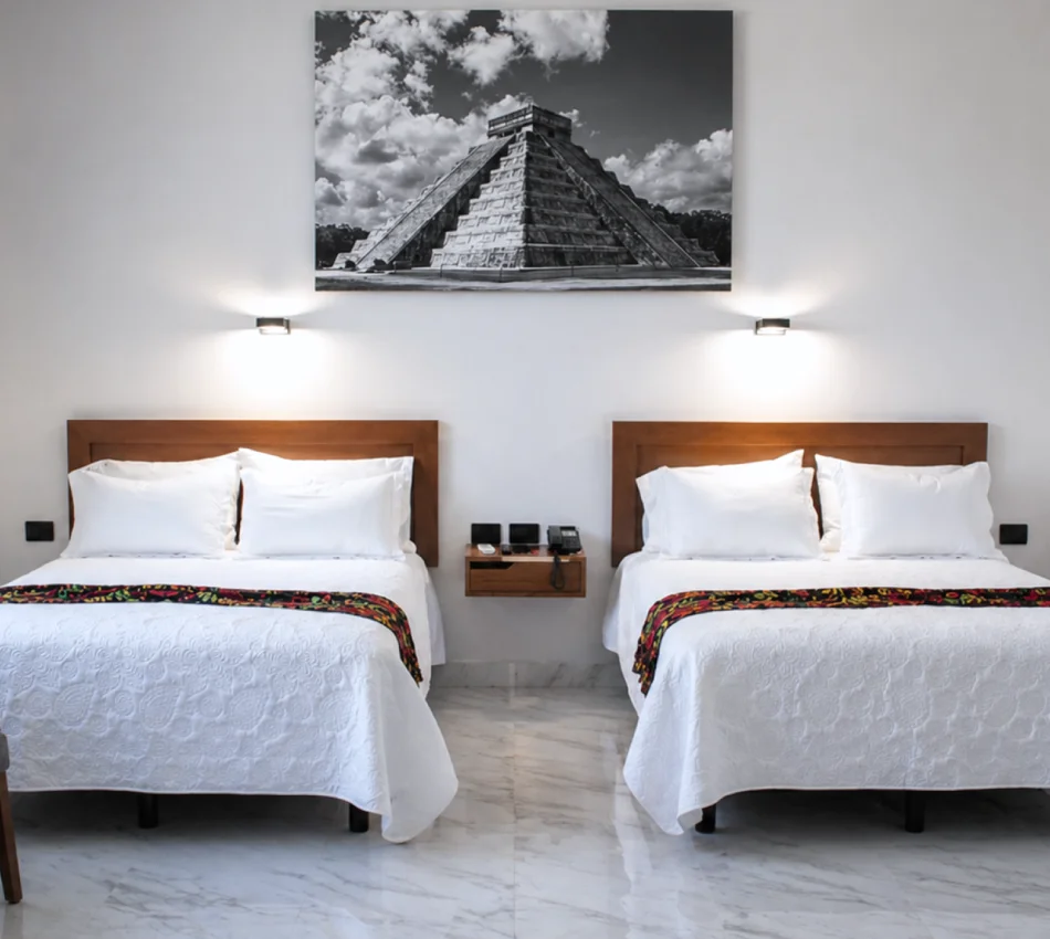 Dos camas gemelas con s&aacute;banas blancas en una habitaci&oacute;n, con cuadro en blanco y negro.