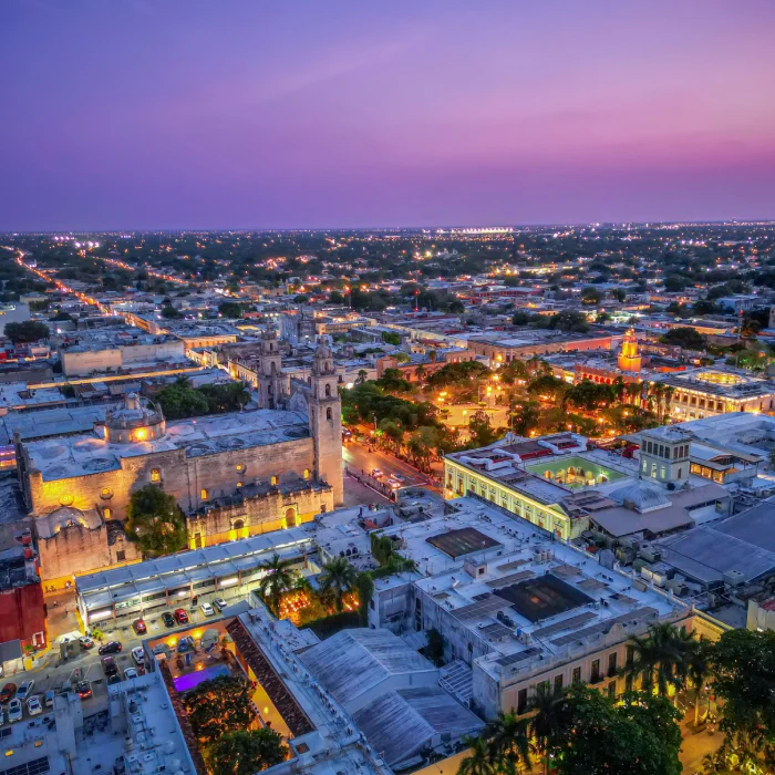 Vista a&eacute;rea al atardecer de una ciudad hist&oacute;rica con iglesias y luces nocturnas.