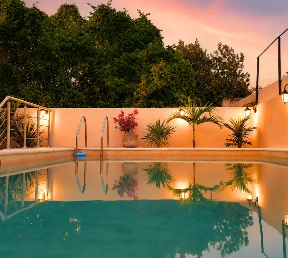 Piscina con palmeras y plantas, reflejo al atardecer, patio iluminado