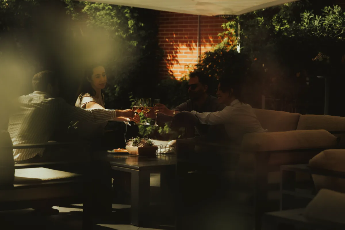 Personas brindando con copas en un patio, bajo una p&eacute;rgola iluminada