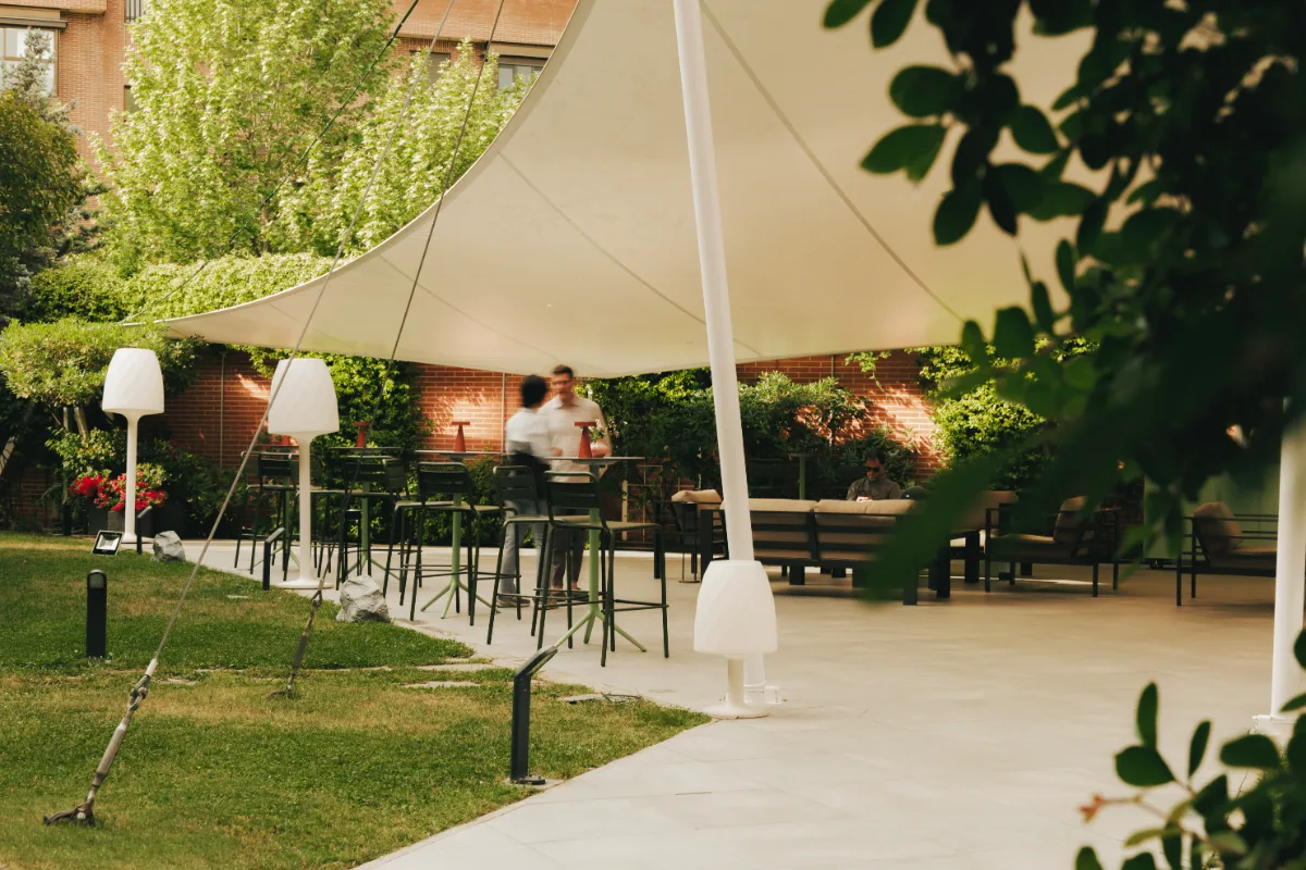 Jard&iacute;n con velas, mesas y sombra de carpa blanca en patio verde.